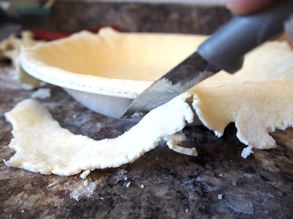 Trimming the edges to pie dough in pie dish.